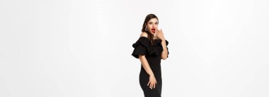 Zarif elbiseli ve kırmızı dudaklı bir kadın, şaşırmış görünüyor, Noel tatilinde hediyeler alıyor, beyaz arka planda hediyeler sunuyor..