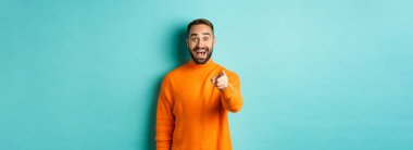 Şaşırmış adam mutlu bir şekilde kameraya bakıyor, birini tanıyor, bir şey gördüğü için heyecanlı, açık mavi arka planda duruyor..