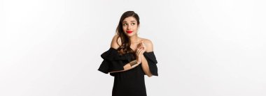 Moda ve güzellik. Siyah elbiseli genç aptal kadın somurtuyor ve ürkek görünüyor, siyah cazibeli elbiseler içinde beyaz arka planda duruyor..