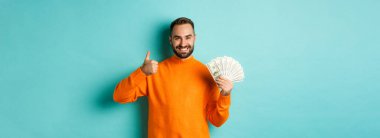 Alışverişe. Mutlu bir adam ortaya çıkıyor ve para dolar şeklinde, banka kredisi veya kredi öneriyor, açık mavi arka planda duruyor..