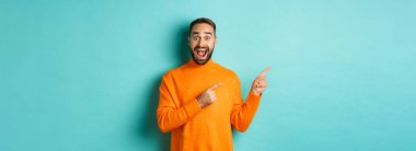 Heyecanlı adam harika bir tanıtım teklifi sunuyor, parmaklarını turkuaz arka planda fotokopi alanına gösteriyor..