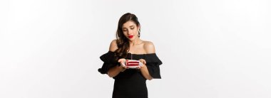 Parti ve kutlama. Kırmızı dudaklı, siyah elbiseli, elinde mumla doğum günü pastası tutan ve rüya gibi görünen, dilek tutan, beyaz arka planlı, tatlı genç bir kadın..