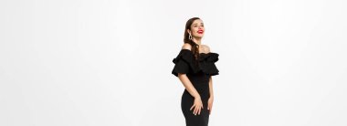 Lüks elbiseli, kırmızı dudaklı ve takılı güzel bir kadının dikey görüntüsü. Beyaz arka planda duran Noel hediyeleriyle birlikte..