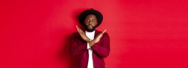 Ciddi siyahi adam görüntüsü buna şiddetle karşı çıkıyor, çapraz işaret gösteriyor, bir şeyi yasaklıyor, kırmızı arka planda duruyor..