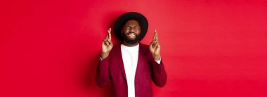 Umut dolu Afrikalı Amerikalı bir adam dilek tutuyor, şans diliyor ve iyimser gülümsüyor, kırmızı parti geçmişine karşı duruyor..