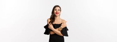 Moda ve güzellik. Güzel, mutlu bir kadın iki seçenek gösteriyor, gülümsüyor, siyah elbise giyiyor, beyaz arka plan..