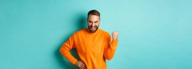 Tatmin olmuş genç bir adamın resmi. Kazandığını hisseden, yumruk tokuşturan ve memnuniyetle evet diyen, hedefe ulaşan, açık mavi arka planda ayakta durarak zafer kazanan..