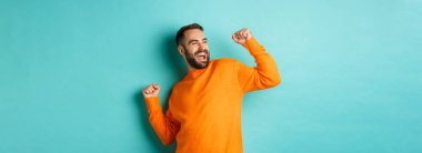 Mutlu adam kolunu kaldırıyor, kazanan gibi hissediyor, zaferi kutluyor, açık mavi arka planda duruyor..