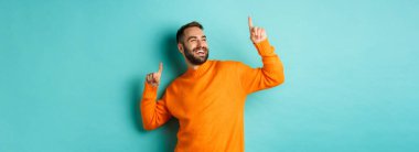 Yakışıklı adam kutlama yapıyor, kazandığını hissediyor, parmaklarını havaya kaldırıyor ve açık mavi arka planda dans ediyor..