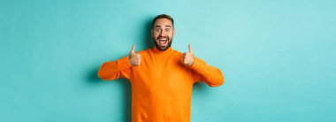 Hayret verici bir adam açık mavi arka planda duran harika bir şeyi onaylıyor ve övüyor..