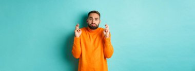 Umut dolu üzgün adam bir dilek diliyor, şans diliyor ve somurtuyor, turkuaz arka planda duruyor..