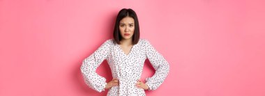 Sevimli alıngan kız kaşlarını çatıyor, el ele tutuşuyor ve kameraya bakıyor hayal kırıklığına uğramış, üzgün ve kasvetli pembe arka plan üzerinde duruyor..