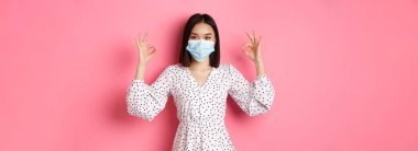 Coronavirus, sosyal uzaklık ve yaşam tarzı konsepti. Yüz maskesi takmış tatmin olmuş Asyalı bir kadın. Onaylıyor ve onaylıyor. İyi seçimi övüyor..