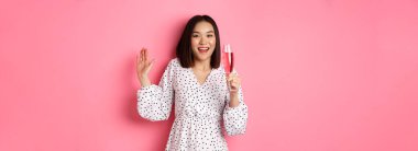 Kutlama. Güzel Asyalı kadın şampanya içiyor ve gülümsüyor, pembe arka planda dikiliyor..