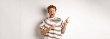 Kızıl saçlı neşeli adam reklam ofisini kontrol ediyor, logoyu sola doğrultuyor ve kameraya gülümsüyor, beyaz arka planda duruyor..