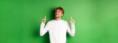 Gözlüklü neşeli yakışıklı adam satış anlaşmasını kontrol ediyor, mutlu ve rüya gibi bir gülümsemeyle yukarı bakıyor, yeşil arka planda duruyor..