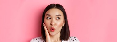 Güzellik ve yaşam tarzı konsepti. Şaşkın Asyalı kadının yakın çekimi solda, alışveriş promosyonuna bakıyor, pembe arka planda duruyor..