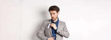 İş adamı kredi kartını takım elbisenin cebine koyar ve ıslık çalar, alışveriş yapar, beyaz arka planda durur..