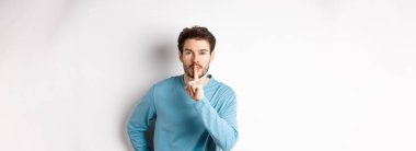 Çekici sakallı bir adam sessiz kalmak istiyor. Tabu işareti yapıyor. Sakin bir şekilde kameraya bakıyor..