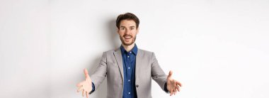 Takım elbiseli mutlu yakışıklı adam, iş ortaklarını karşılamak için ellerini uzat, konukları karşıla, heyecanlı bir şekilde gülümse, beyaz arka planda dur..