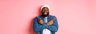 Heyecanlı genç Afro-Amerikalı adam iki seçenek gösteriyor ve karar veriyor, mutlu bir şekilde gülümsüyor, pembe arka planda duruyor..