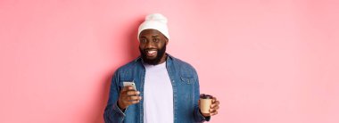 Tarz sahibi siyahi bir hippinin kahve içerken, telefonla mesaj okurken, gülümserken, pembe arka planda dururken görüntüsü..