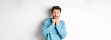 Korkudan titreyen korkmuş genç bir adamın görüntüsü, yüzünün yanında el ele tutuşmuş ve kameraya bakarken ürkmüş, beyaz arka planda duruyor..