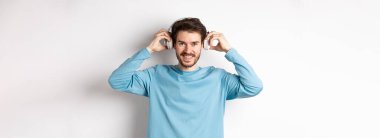 Adam müzik ya da podcast dinlemek için kablosuz kulaklık takmış, kameraya gülümsüyor, pembe arka planda duruyor..