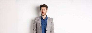 Şok olmuş takım elbiseli girişimci beyaz arka planda duran ürkmüş yüzüyle logoya bakıyor..