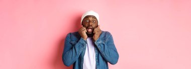 Korkmuş ve ürkmüş siyah adam soluk soluğa, kameraya yan yana bakıyor, pembe arka planda şoke olmuş duruyor..