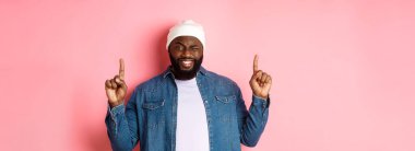 Yüzsüz Afrikalı Amerikalı adam gülümsüyor ve göz kırpıyor. Anlaşmayı üstte gösteriyor. Parmakla işaret ediyor, pembe arka planda duruyor..