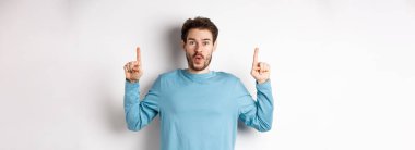 Şaşırmış genç bir adam en iyi reklamını yapıyor, yukarı bakıyor ve kameraya 