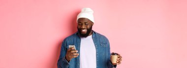 Tarz sahibi siyahi bir hippinin kahve içerken, telefonla mesaj okurken, gülümserken, pembe arka planda dururken görüntüsü..