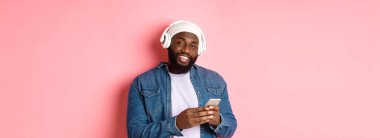 Kulaklıklı yakışıklı hippi kameraya gülümsüyor, kulaklıkla müzik dinliyor, mobil uygulama kullanıyor, pembe arka planda duruyor..