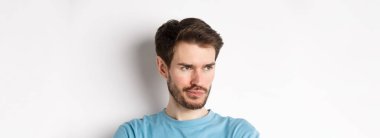 Hayal kırıklığına uğramış sakallı adamın yakın çekimi, somurtuyor ve düşünceli bir yüz ifadesiyle sol tarafa bakıyor, beyaz arka planda üzgün duruyor..