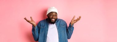 Siyahi bir adam omuz silkiyor ve kameraya bakıyor. Bilmiyorum, pembe arka planda kararsız duruyor..