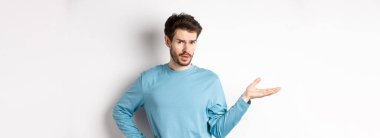 Ne olmuş yani? Kafası karışmış genç adam elini kaldırıyor ve kameraya şüpheci bakıyor, hiçbir şey bilmiyor, bir şey anlayamıyor, beyaz arka planda duruyor..