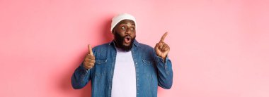 Mutlu Afro-Amerikalı adam baş parmağını yukarı kaldırıyor ve sol üst köşedeki fotokopi alanını işaret ediyor, iyi bir anlaşmaya övgüler yağdırıyor, pembe arka planda duruyor..