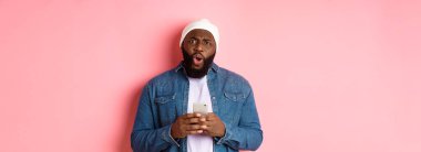 Teknoloji ve online alışveriş konsepti. Kafası karışmış ve hayal kırıklığına uğramış Afro-Amerikan adam şikayet ediyor, cep telefonunu tutuyor ve kameraya bakıyor..