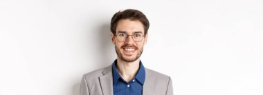 Gözlüklü, takım elbiseli, kameraya gülümseyen, beyaz arka planda mutlu görünen genç ofis çalışanlarının yakın çekimi..