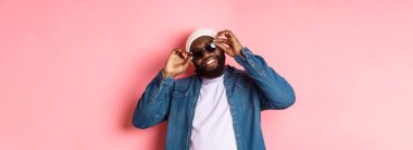 Yakışıklı Afro-Amerikalı adam güneş gözlüğü taktı, gülümseyen, kendinden emin, pembe arka plana karşı duran. Boşluğu kopyala