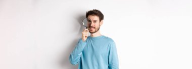 Gülümseyen genç dedektif büyüteçle bakıyor, tanıtım teklifi arıyor, beyaz arka planda duruyor..