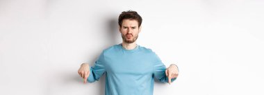 Surat asan adam kötü bir şeyi işaret ediyor, kaşlarını çatıyor ve şikayet ediyor, beyaz arka planda duruyor..