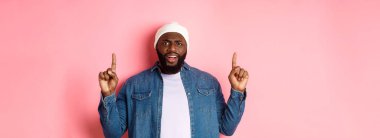 Hayal kırıklığına uğramış ve üzgün siyah adam kaşlarını çatmış, parmaklarını kaldırmış ve kameraya bakıyor rahatsız, şikayet ediyor, pembe arka planda duruyor..