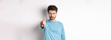 Sakallı, parmağını sallayarak onaylamadığı, bir şeyi yasakladığı ya da yasakladığı beyaz arka planda duran ve hayır diyen ciddi bir gencin görüntüsü..