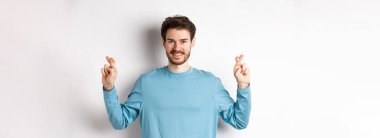 İyimser gülümseyen adam şans diliyor, dilek diliyor ve sonuçları bekliyor, beyaz arka planda duruyor..