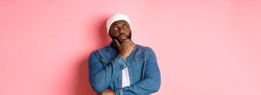 Düşünceli Afro-Amerikan erkek model karar veriyor, düşünüyor ve sol üst köşeye bakıyor, seçiyor ya da düşünüyor, pembe arka planda duruyor..