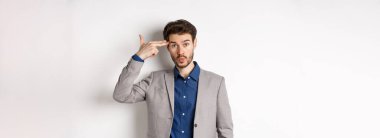 İş elbisesi giymiş sinirli bir adam kafasına silah dayamış, işten sonra üzgün ve yorgun görünüyor, beyaz arka planda duruyor..