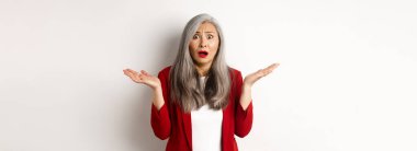 İş adamları. Kafası karışmış ve endişeli Asyalı üst düzey ofis hanımı endişeli görünüyor, ellerini yana açmış şaşkın, beyaz arka planda dikiliyor..