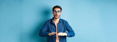 Gözlükçüde güneş gözlüğü deneyen, dans eden ve eğlenen, mavi arka planda duran komik adam..